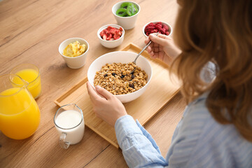 Young woman with bowl of tasty granola and freeze-dried berries in bowls on table at home