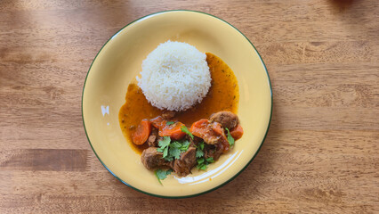 Plate of beef stew with carrots and white rice on wooden table