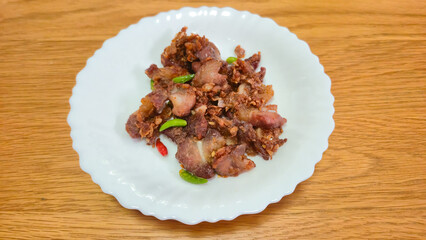 Fried pork with chili peppers served on white plate on wooden table