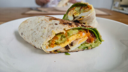 Vegetarian wrap sandwich with fresh vegetables and avocado on white plate