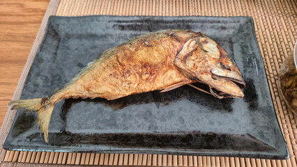 Grilled Thai mackerel fish served on a black rectangular plate on bamboo mat
