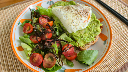 Poached egg on avocado toast with fresh salad on a plate for healthy breakfast