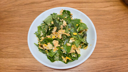 Stir-fried Malindjo Leaves with Egg on white plate on wooden table Thai food