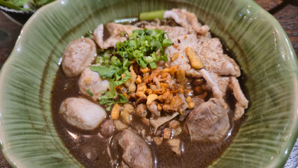 Thai boat noodle soup with pork meatballs and herbs in green bowl