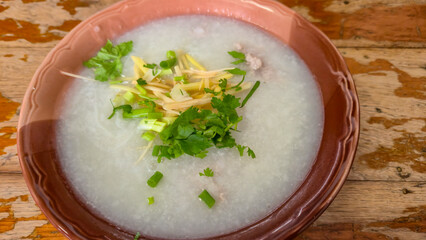 Traditional rice porridge with herbs and ginger served in ceramic bowl on wooden table