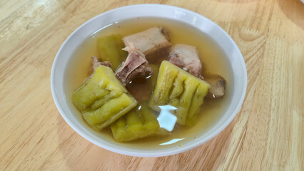 Thai Bitter melon soup with pork ribs in white bowl on wooden table, Thai food