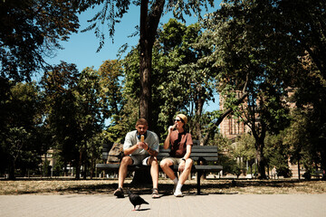 Young man and woman sitting together on a bench in the park eating ice cream and talking. Concept of friendship, leisure, and summer lifestyle