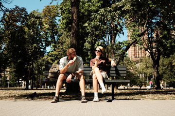 Young man and woman sitting together on a bench in the park eating ice cream and talking. Concept of friendship, leisure, and summer lifestyle