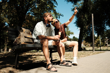 Young man and woman sitting on a park bench eating ice cream while the woman points at something. Concept of friendship, joy, and summer freedom