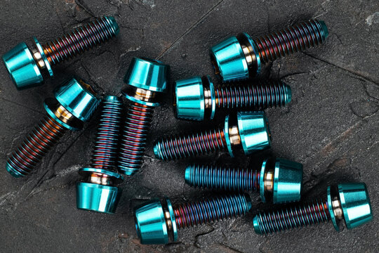 Screws made of blue-purple anodized titanium alloy on a black textured background