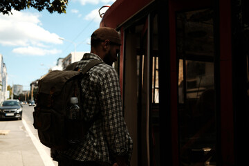 Male traveler entering a red city tram with backpack. Concept of public transport, urban mobility, and daily life
