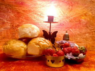 Buns, strawberries, berries, food. Lilac flowers. Evening romantic still life on a red background, candle in a candlestick. Romance, flowers, elegance, flair. Antique brass items