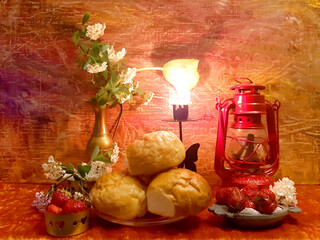 Buns, strawberries, berries, food. Vase, lantern. Lilac flowers. Evening romantic still life on a red background, candle in a candlestick. Antique brass items