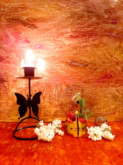 Lilac flowers, strawberries, miniature violin figurine. Evening romantic still life on a red background, candle in a candlestick. Antique brass items