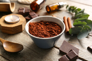 Spa composition with bowl of cocoa powder and pieces of chocolate on wooden background, closeup