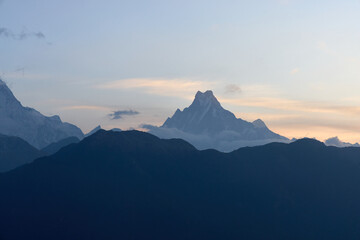 Majestic mountain range featuring Machhapuchhre peak against a soft sunrise sky with beautiful pastel hues during trekking in the Himalayas, Nepal.