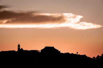 Fototapeta premium Scenic view of Montilla, a Spanish town at sunset, with the church tower and rooftops silhouetted against a warm orange sky and dramatic cloud.