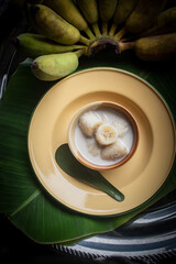 Kluay Buat Chi, a traditional Thai dessert made from ripe bananas cooked in rich coconut milk, served in a ceramic bowl with natural light still life style.