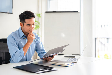 Confident young businessman auditing revenue report and planning budget while working at desk in office.