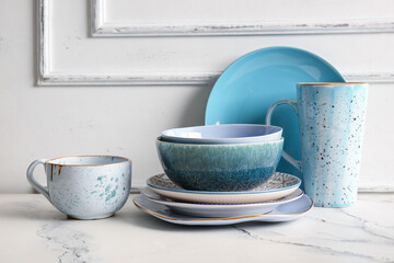 Clean dishes on marble table near white wall