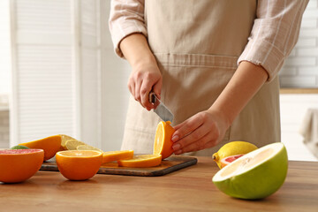 Young woman cutting orange on table in kitchen, closeup
