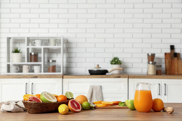 Tasty citrus fruits and jug of fresh juice on table in kitchen
