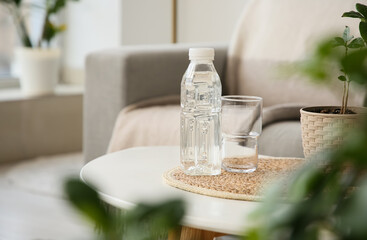 Bottle of water, glass and houseplant on table in room,