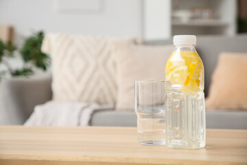 Bottle of water with pieces of lemon on table in room, closeup