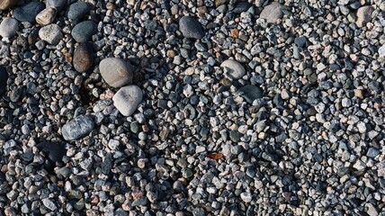 a close-up view of a gravel surface composed of small, variously sized gray and white black stones and pebbles with white and brown hue, creating speckled texture