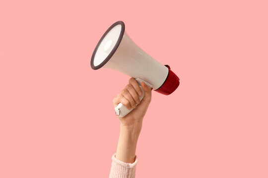 Female hand holding megaphone on pink background