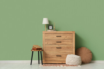 Lamp and alarm clock on chest of drawers near green wall in interior of living room