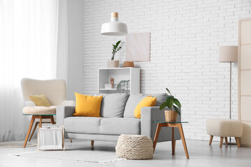 Interior of living room with sofa and pouf near white brick wall