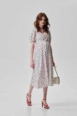 A girl model in stylish clothes poses on a gray background.