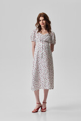 A girl model in stylish clothes poses on a gray background.