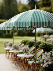 Obraz premium Vintage green and white striped umbrella shades outdoor cafe tables with floral arrangements, creating charming and inviting garden setting