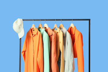 Black rack with stylish clothes on blue background, closeup
