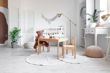 Comfortable crib, table, chairs and lamps near white wall in interior of children's room