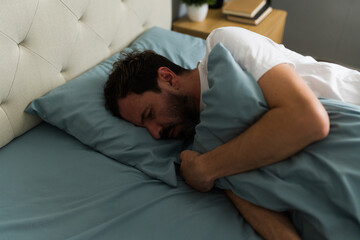 Sad man suffering from insomnia and hugging pillow in bed