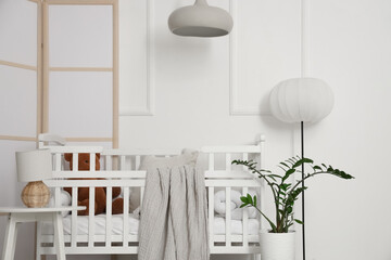 Floor lamp and comfortable crib near white wall in interior of children's room, closeup
