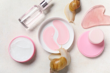 Giant Achatina snails, under-eye patches, guasha tool, bottle and jars of cosmetic products on white grunge background, closeup