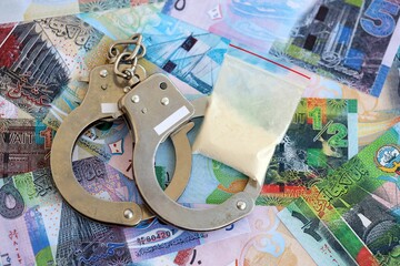 Kuwaiti dinar currency money bills and cocaine pack with handcuffs close up. The concept of drug...