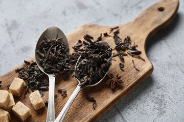 Spoons with dry black tea leaves and cubes of sugar on grey background, closeup