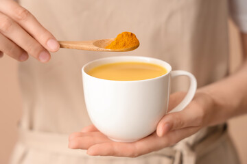 Young woman making turmeric drink on beige background, closeup