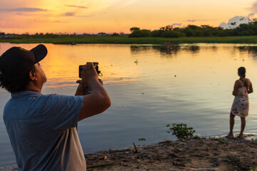 Obraz premium Person taking photos of the Amazon sunset with their cellphone, as the sky glows over the rainy jungle of Peru