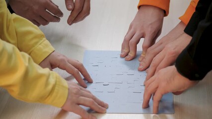 Hands assemble puzzle pieces together showing teamwork and collaboration as group uses cooperation and strategy to solve puzzle by fitting final piece while hands coordinate to complete team task