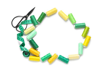 Frame made of many thread spools with scissors and measuring tape on white background