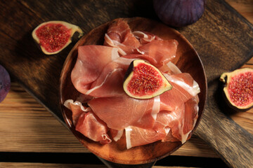 Plate with delicious prosciutto slices and fresh figs on wooden background