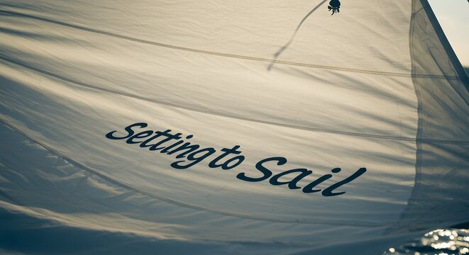 Close-up of a sailboat's white sail with the words "Setting to Sail" printed in black script font