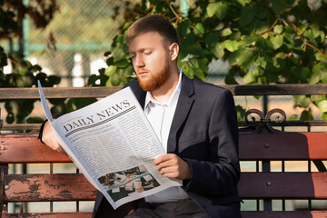 Young businessman reading newspaper on bench in park