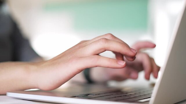 Typing on laptop keyboard with hand poised over keys and fingers tapping keys on computer during work in office setting closeup showing finger movement and device detail for business and technology
